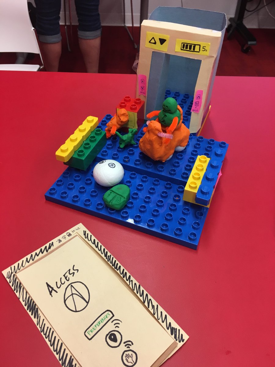 Pictured is group Assorted Barrier Busters prototype. They have used lego blocks to build a platform, craft paper to build an elevator cube and plasticine to create a mobility device, such as an electric scooter and a guide dog. The image also shows their proposed Access app prototype made with craft paper.
