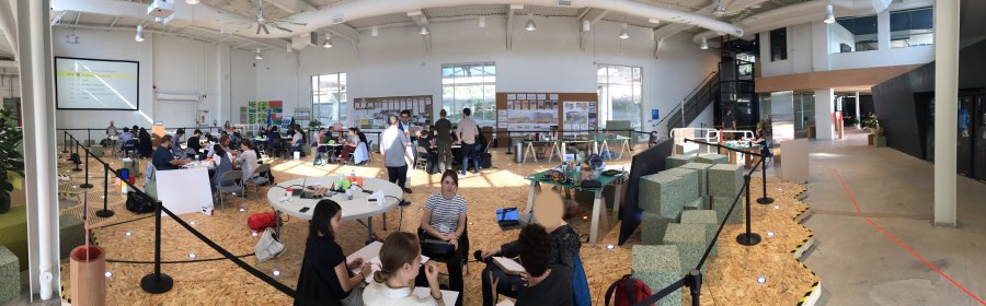The Sidewalk Lab space, with participants sitting on the Dynamic Streets prototype. In the foreground, group Tranquil Refuge is engaging in discussion regarding the design of their idea.